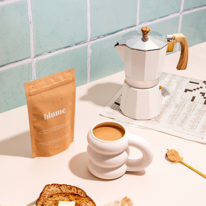 A coffee setup with a moka pot, mug, toasted bread, and a 'blume' beverage mix.